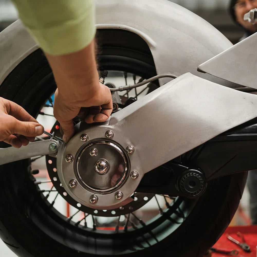 Mechanic adjusting rear wheel of motorcycle with tools, showing custom wheel and suspension parts