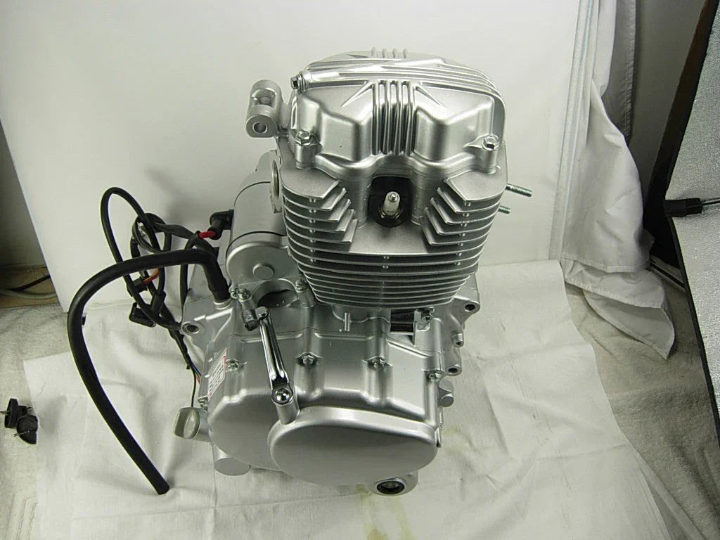 Silver motorcycle engine with cooling fins and black wiring on white fabric background