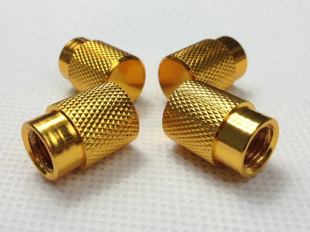Four small gold-colored knurled metal valve caps on white textured surface