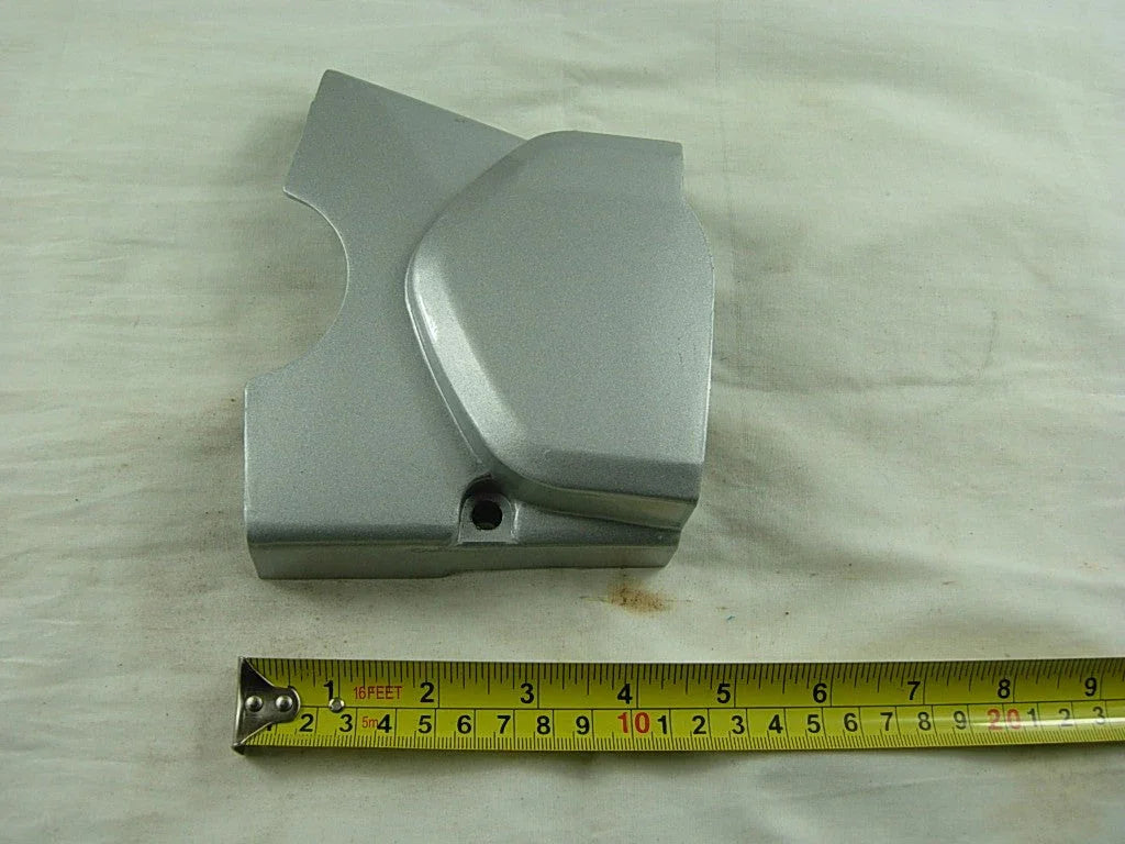 Silver metal engine cover with a measuring tape showing length around 9 inches on a light fabric surface