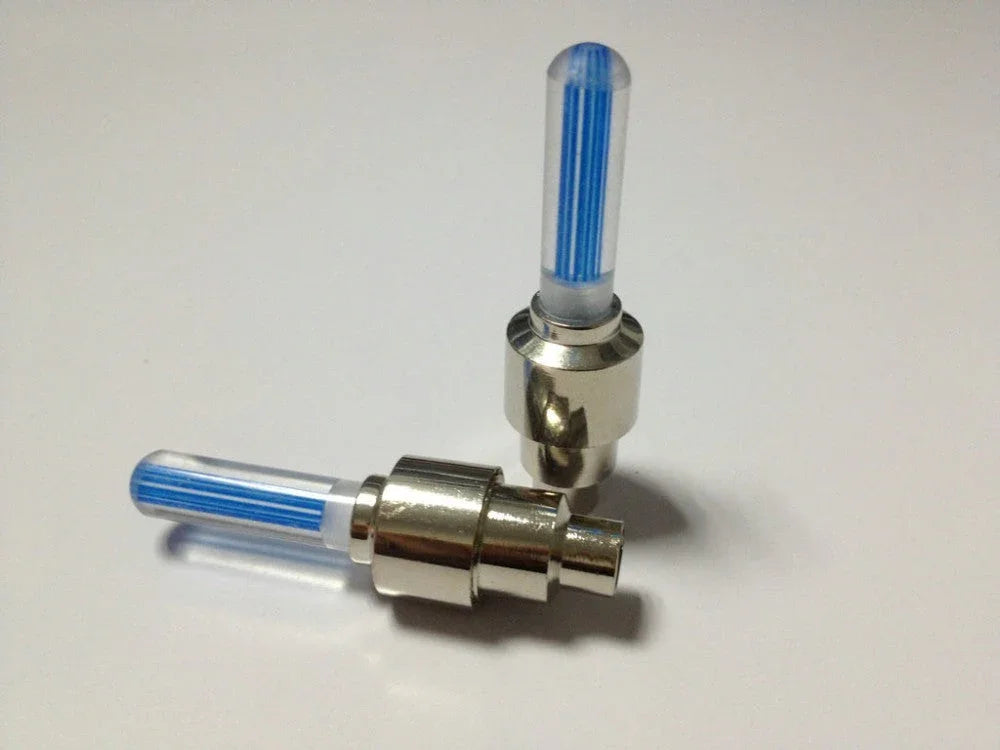 Two metal tire valve caps with blue LED light tubes on a white surface
