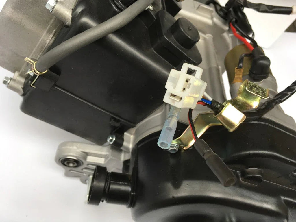 Close-up of motorcycle engine part with black casing, gray wires, and white electrical connector