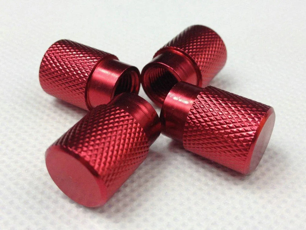 Set of four red metallic knurled valve stem caps with threaded interior on textured white surface