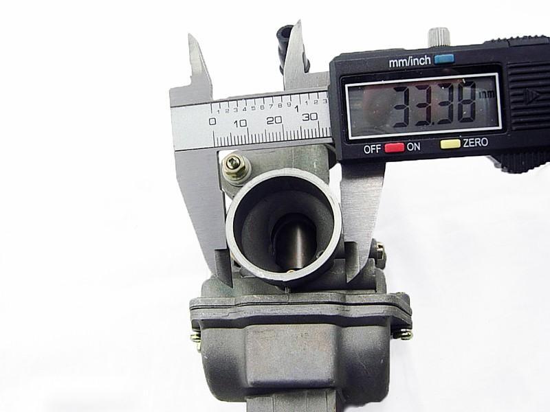 Digital caliper measuring 33.38 mm diameter of a metal carburetor inlet on white background