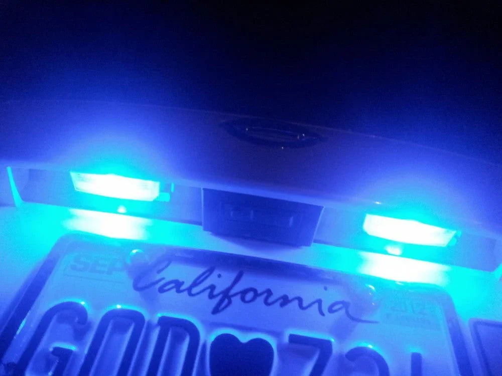Close-up of California license plate illuminated by bright blue LED lights on a white vehicle at night