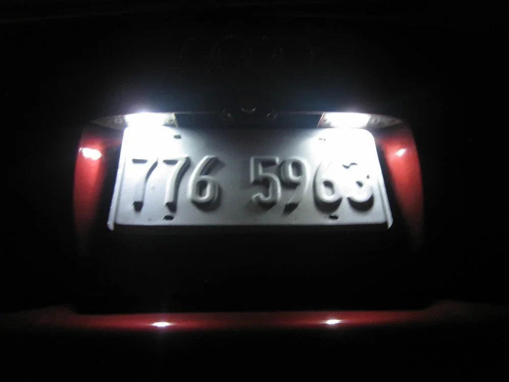 Illuminated white car license plate 776 5963 on red vehicle at night