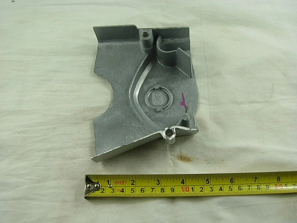 gray metal automotive part with embossed logo, next to yellow measuring tape on beige fabric