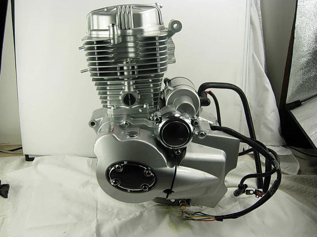 Silver motorcycle engine with black wires on white fabric background in studio setting