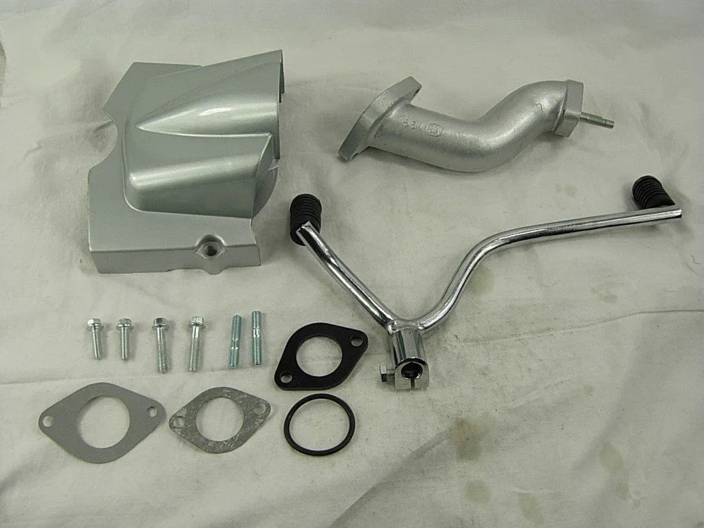 Silver motorcycle engine parts including cover, exhaust pipe, kickstarter lever, gaskets, bolts on white cloth