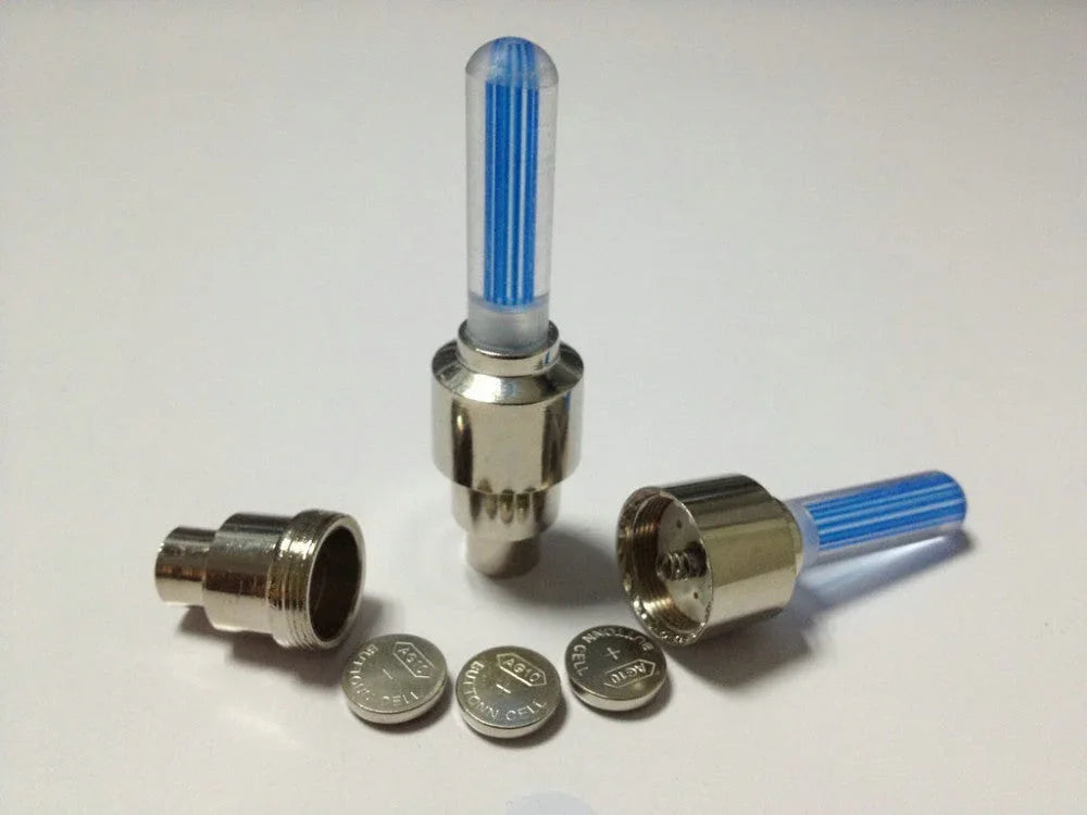 Two disassembled metal LED valve caps with blue light rods and three button batteries on white background