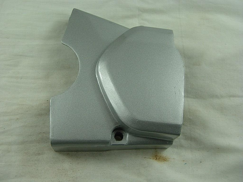 silver metallic engine cover part with curved and angular design on white fabric background