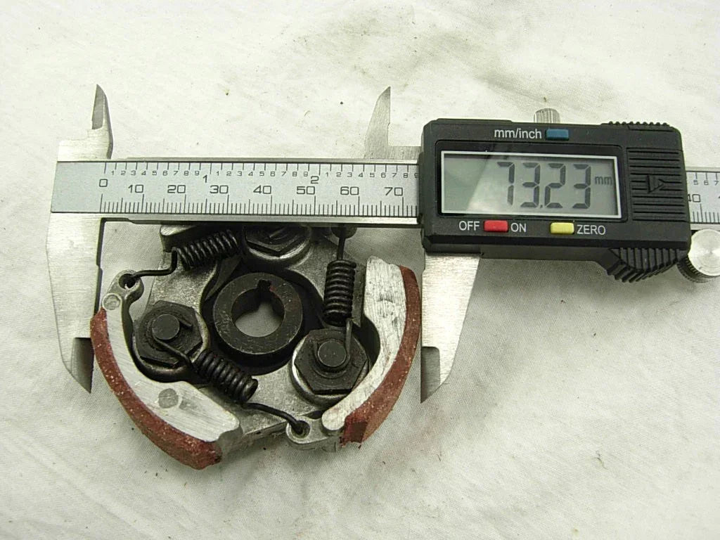 Digital caliper measuring 73.23mm on motorcycle brake caliper with springs and pads