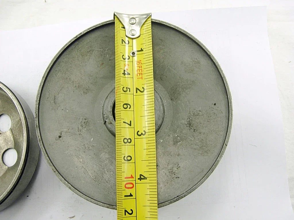 Metal clutch drum measured with a yellow tape measure showing about 4 inches diameter on a white surface