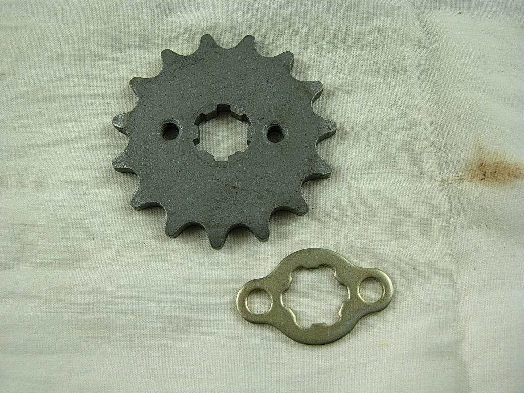 Two metal mechanical parts on a white fabric background with a rust stain, including a gear and a plate