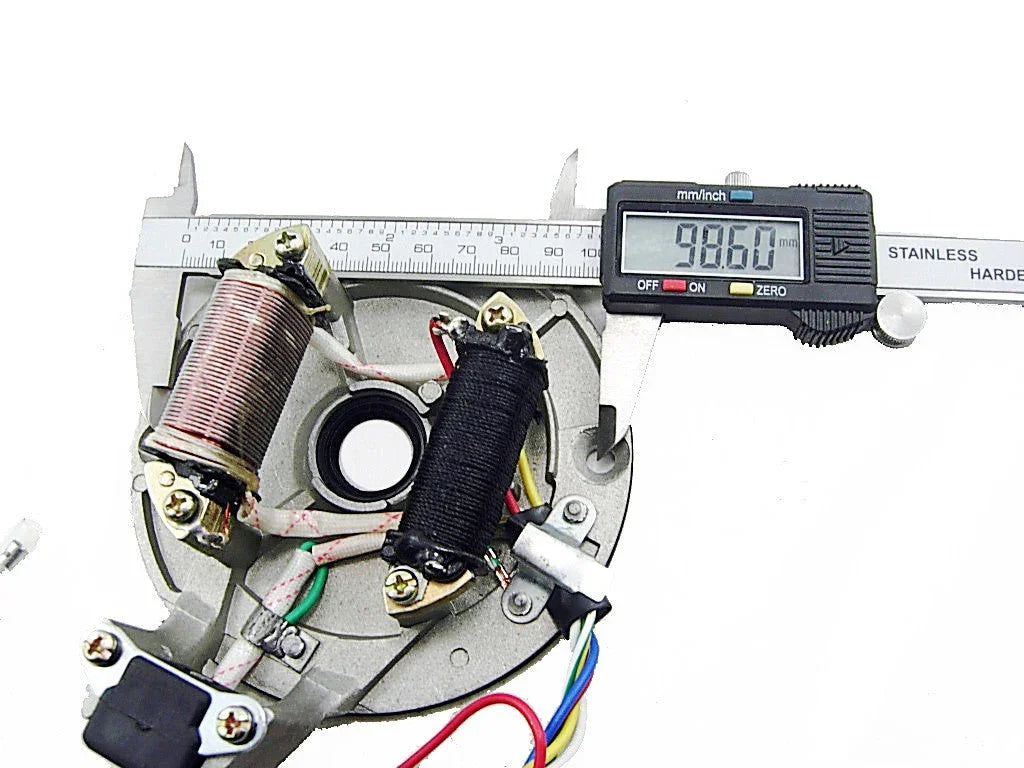 Digital caliper measuring 98.60mm on a motorcycle stator coil with copper and black wire windings