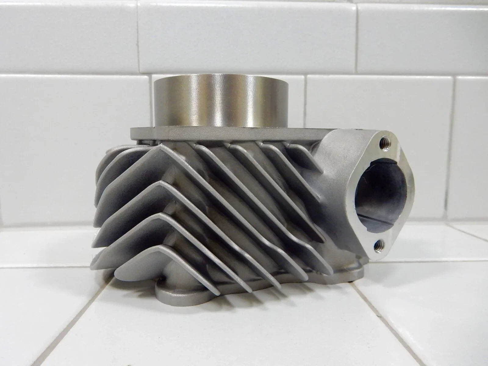 Silver metal engine cylinder head with cooling fins on white tiled surface