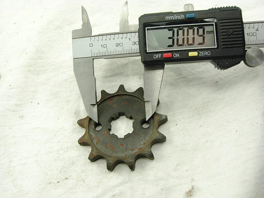 Digital caliper measuring 30.09 mm on a rusty metal sprocket gear with ten teeth on a white surface
