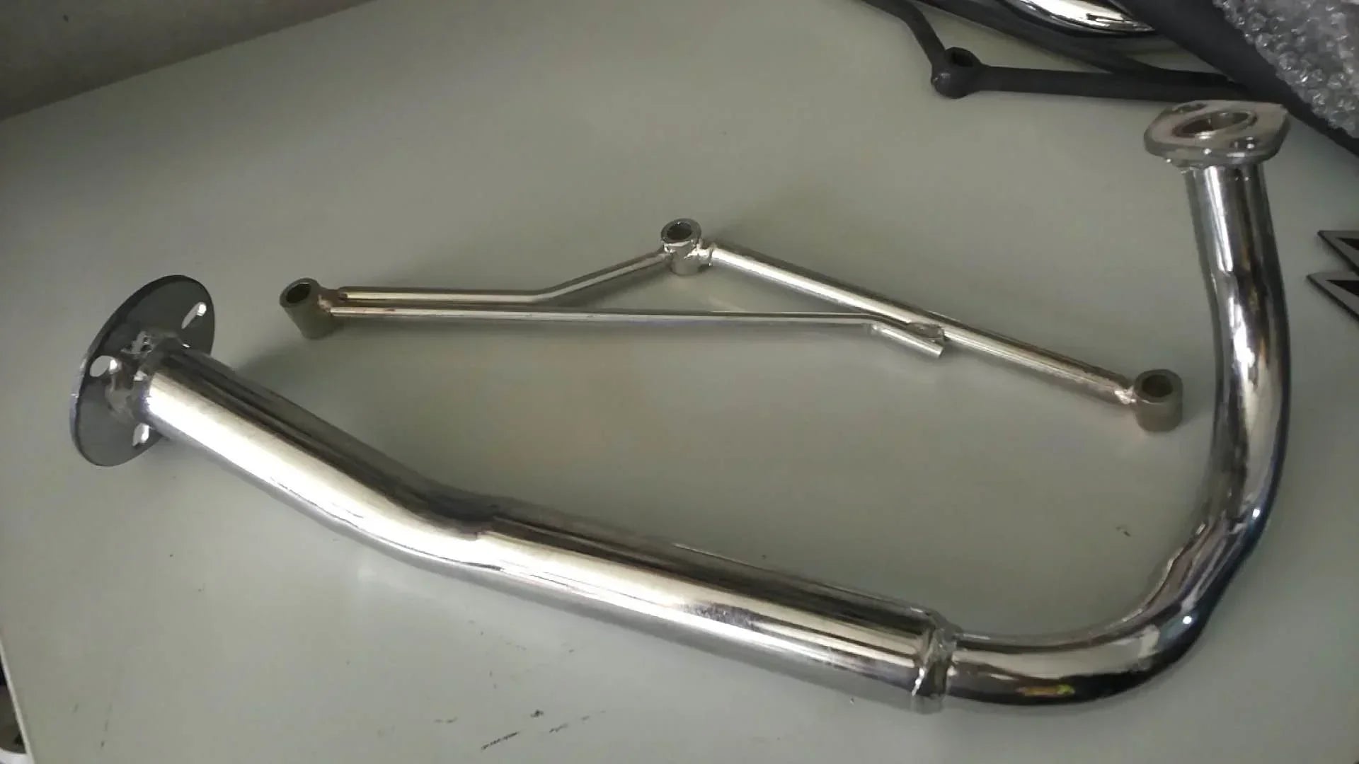 Shiny chrome exhaust pipe for motorcycle or ATV, featuring curved design and mounting flanges