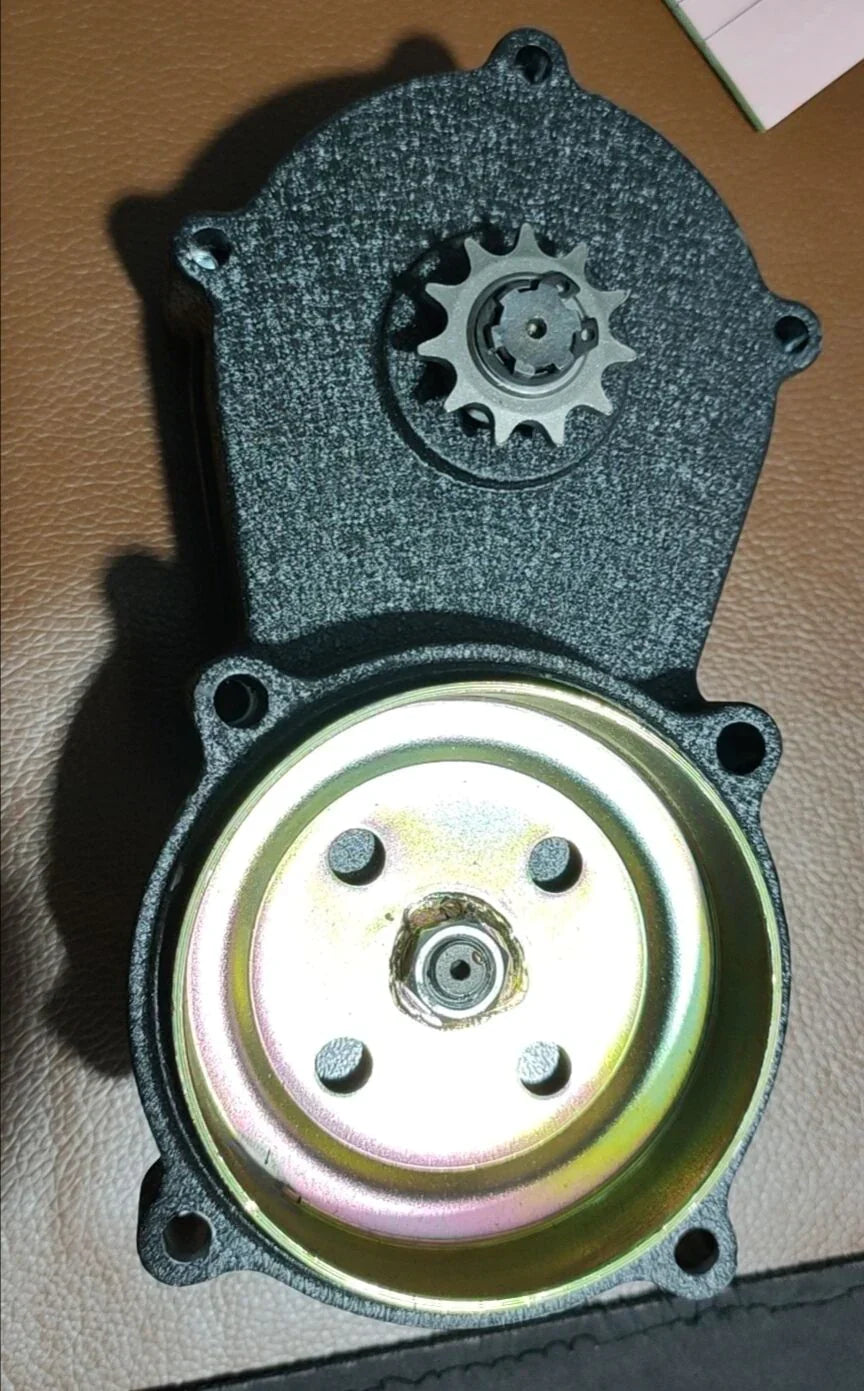 Black mechanical gear housing with a metal sprocket and circular pulley on a brown leather surface