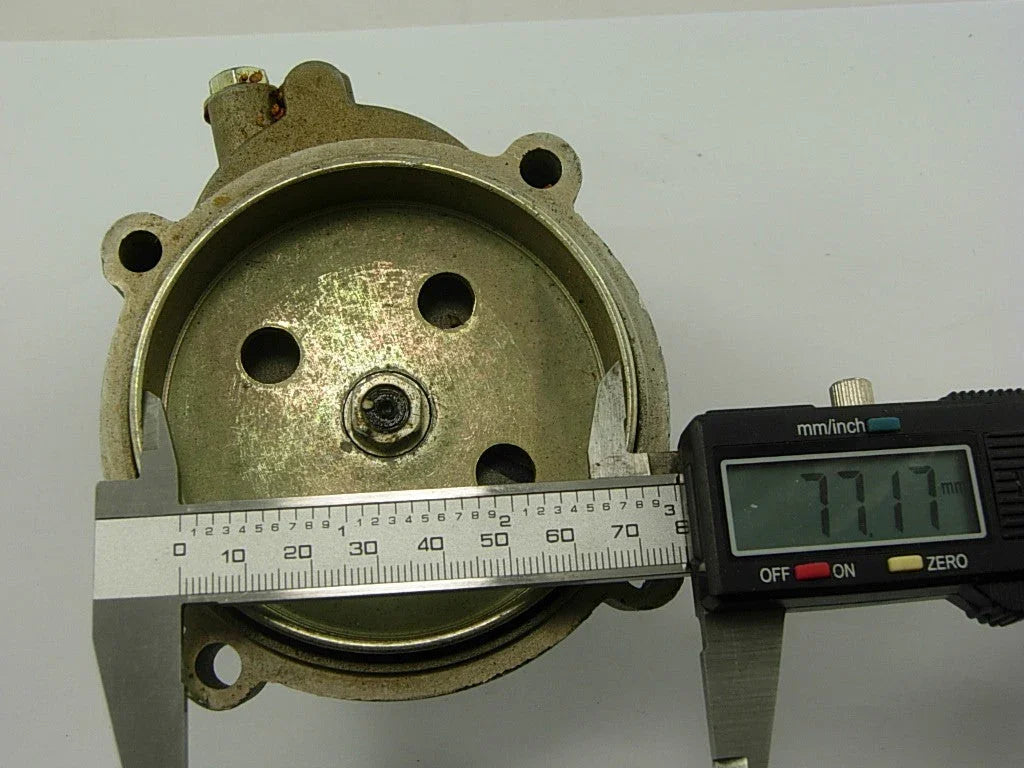 Digital caliper measuring the diameter of a circular metal machine part showing 77.17 mm