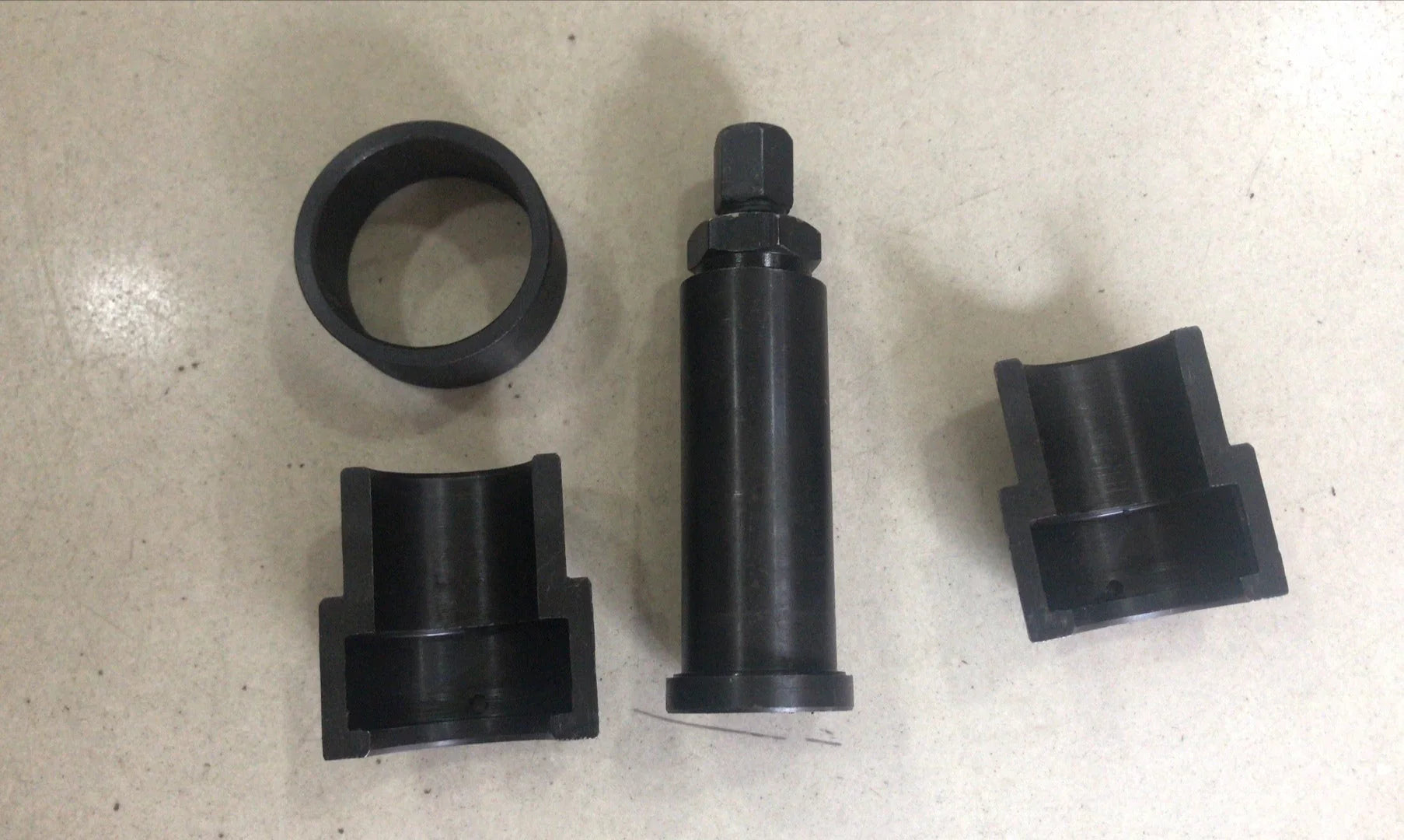 Four black cylindrical metal automotive press tools on a beige surface