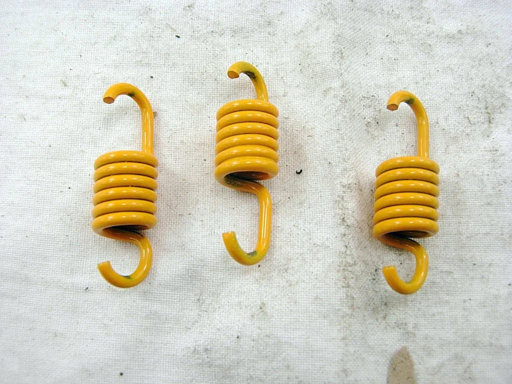 Three yellow coiled metal springs with hooks on both ends on a light textured surface