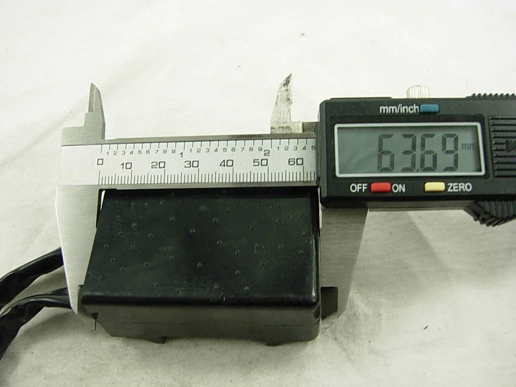 Digital caliper measuring 63.69 mm width of a black electronic component on white surface