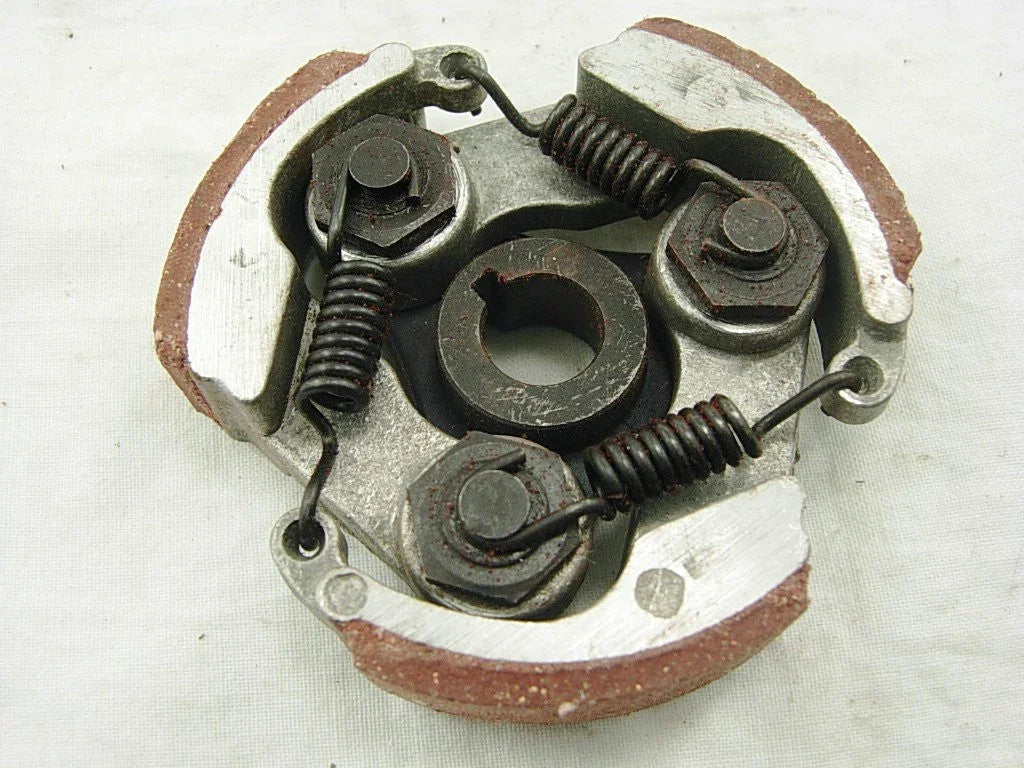 Close-up of a metal centrifugal clutch with springs and friction pads on a white fabric background