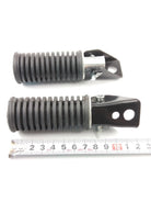Black ribbed motorcycle suspension shock absorbers with mounting brackets, shown with ruler for scale