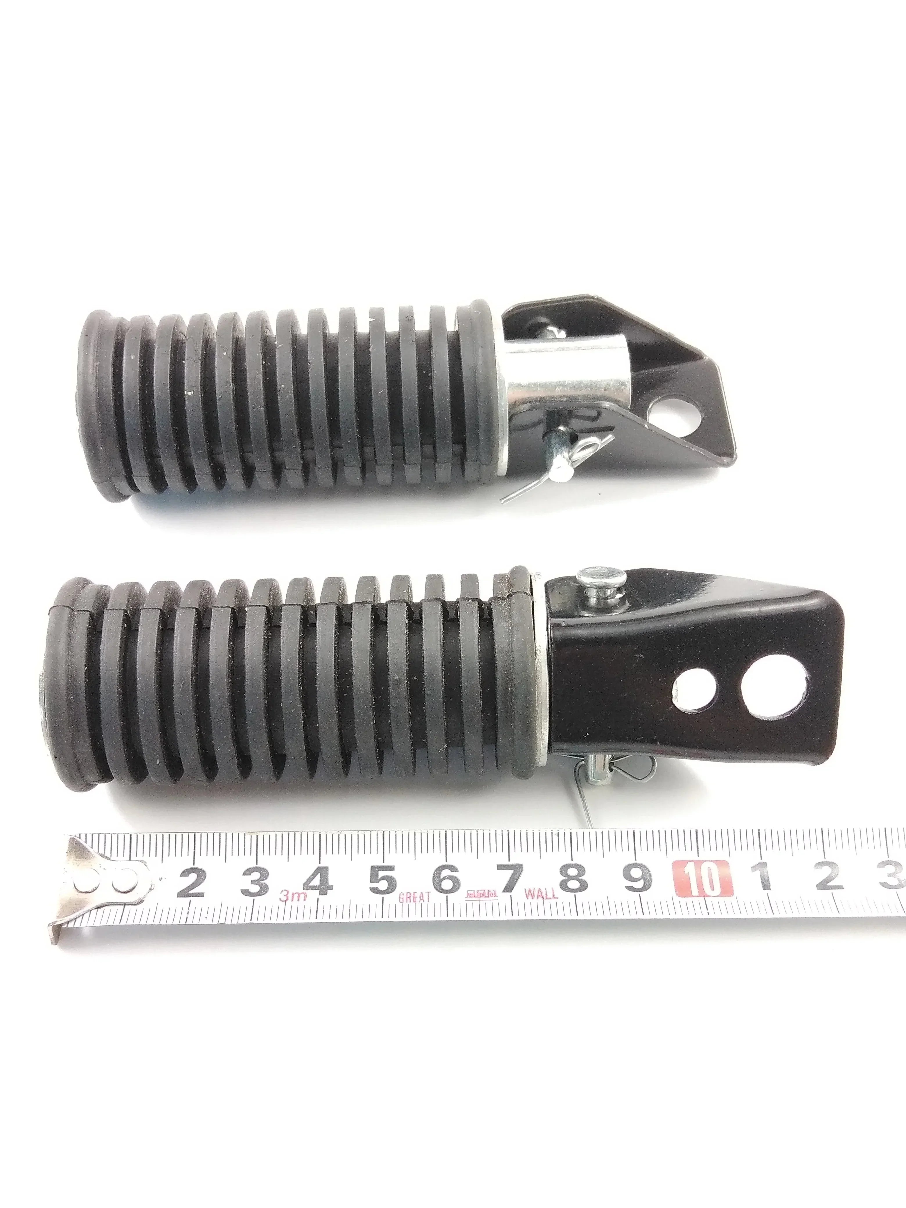 Black ribbed motorcycle suspension shock absorbers with mounting brackets, shown with ruler for scale
