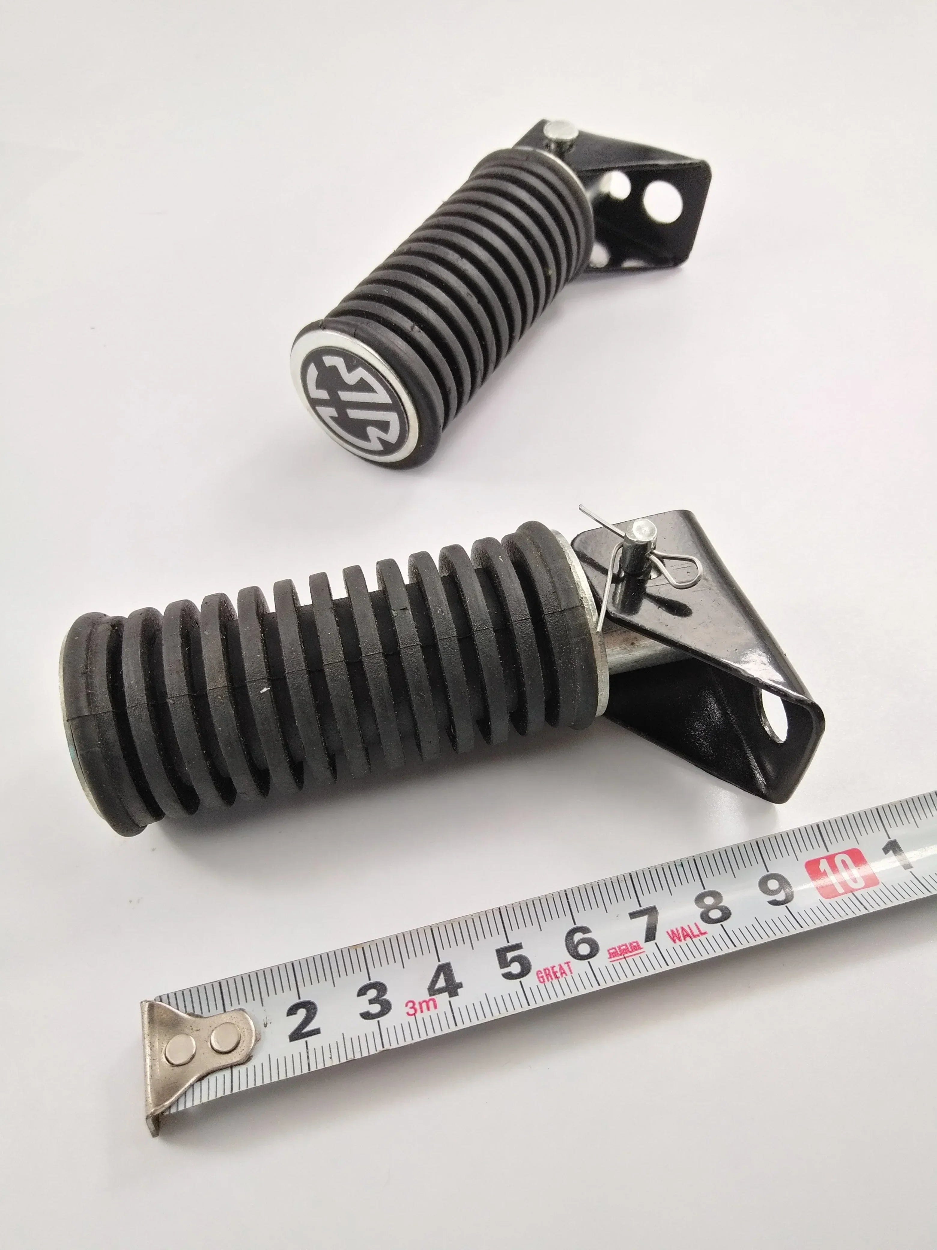 Black ribbed motorcycle suspension spring with metal bracket and measuring tape for size reference