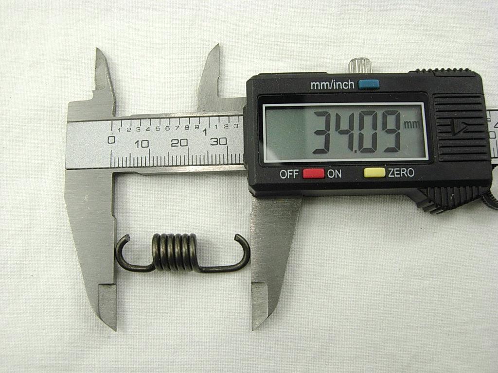 Digital caliper measuring a small coiled metal spring showing 34.09 mm length on white background