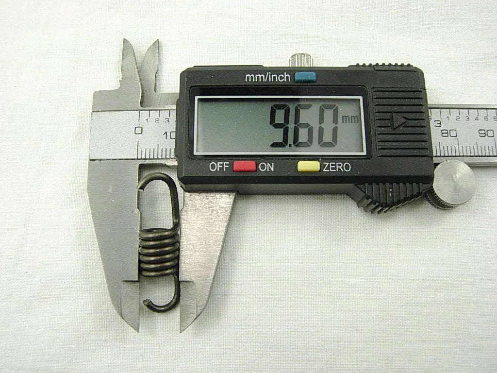 Digital caliper measuring a metal spring showing 9.60 mm length on white background