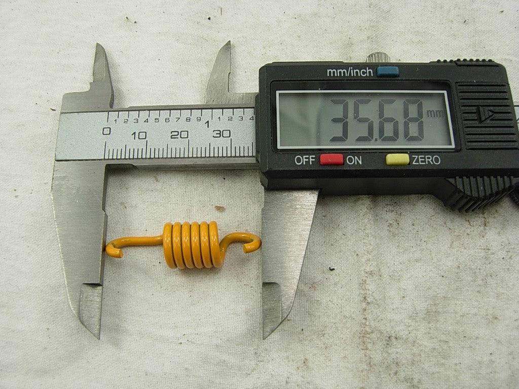 Digital caliper measuring an orange metal spring indicating 35.68 mm length on a white surface