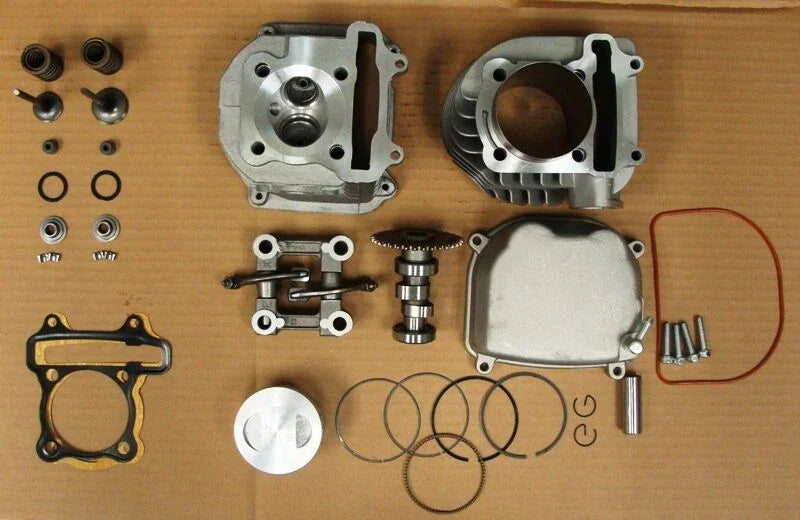 Disassembled motorcycle engine parts laid out on a surface, including piston, cylinder head, cam shaft, gaskets, valves, and bolts