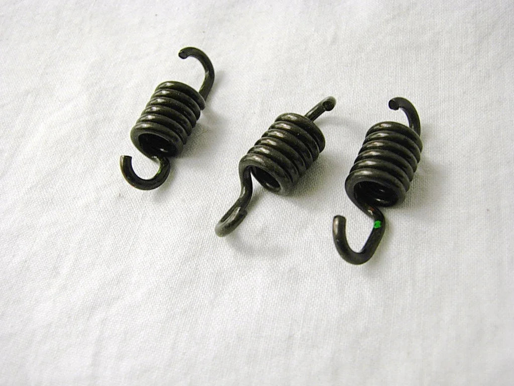 Set of three small black metal coil springs with hooks on white fabric background