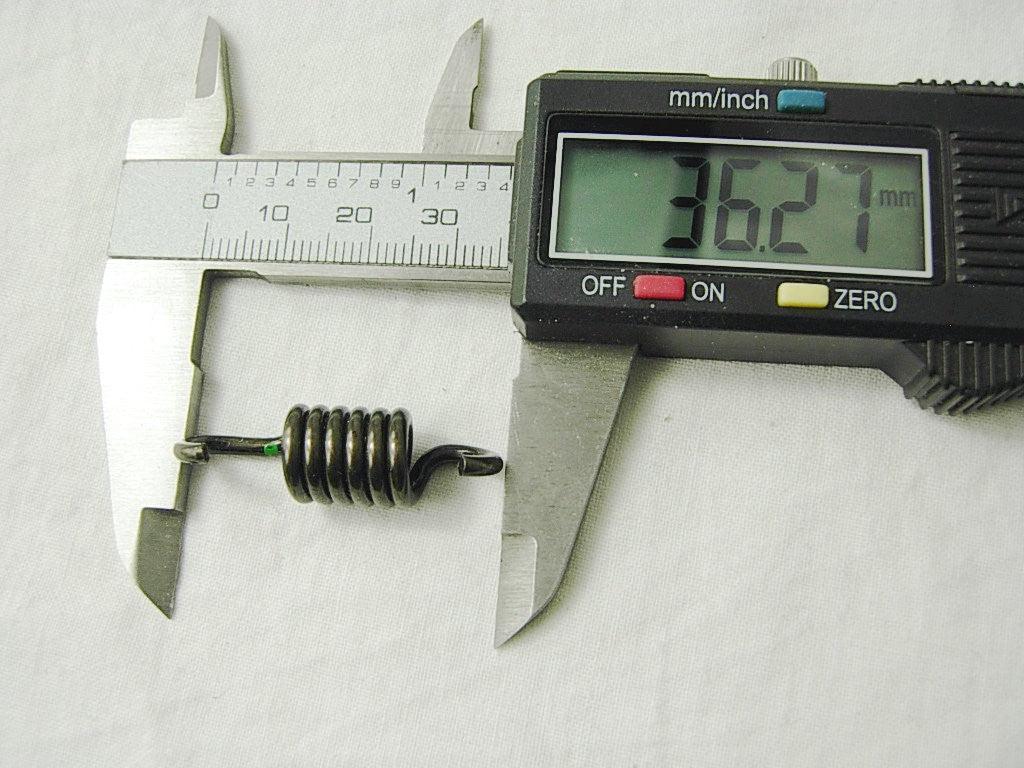 Digital caliper measuring a small black coiled spring, displaying 36.27 mm