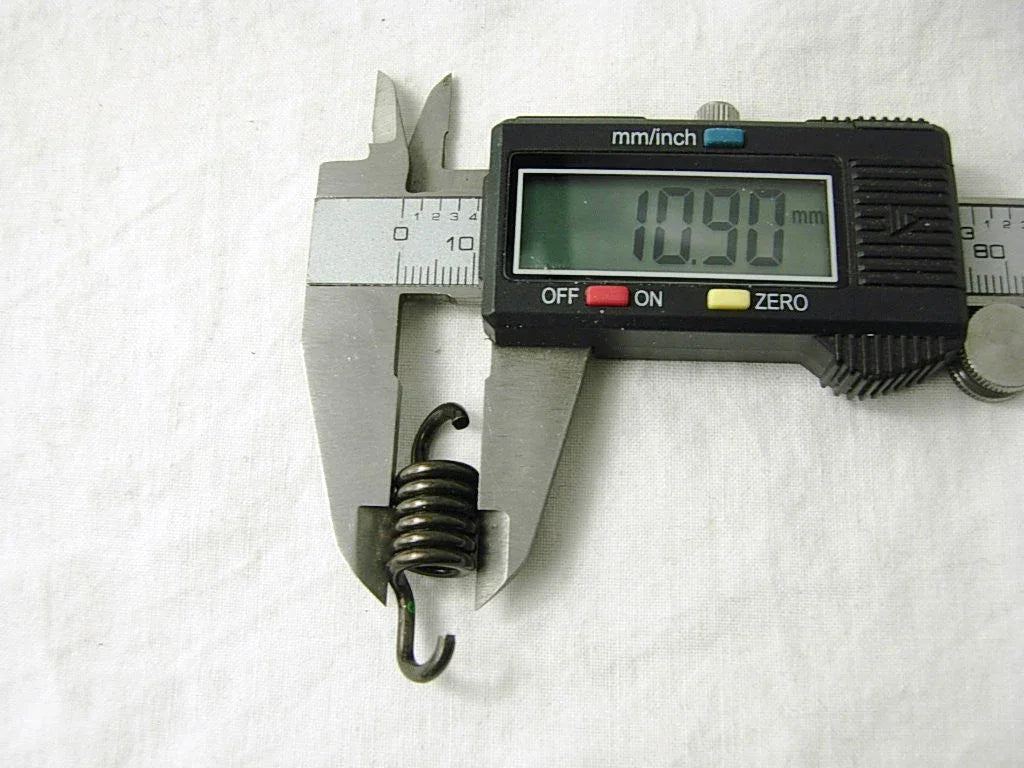 Digital caliper measuring a small metal coil spring showing 10.90 mm on display