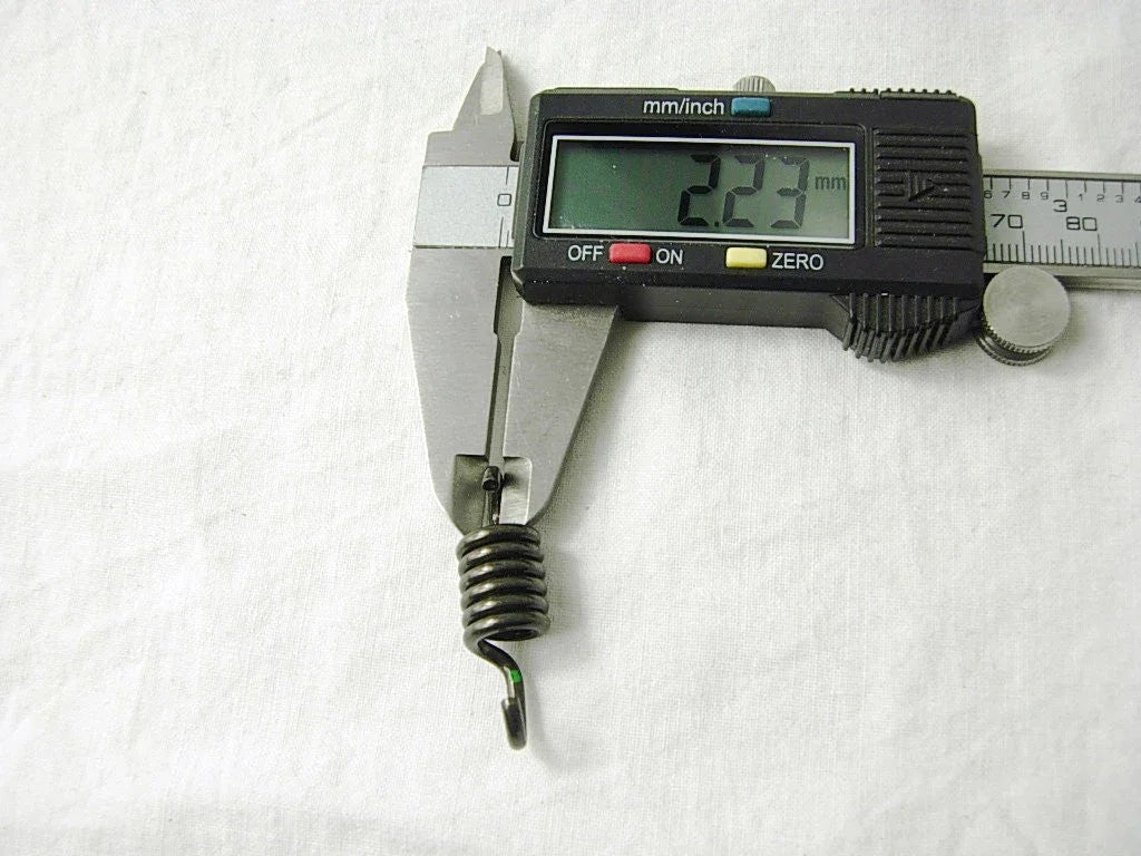 Digital caliper measuring a small metal coil spring showing 2.23 mm on display