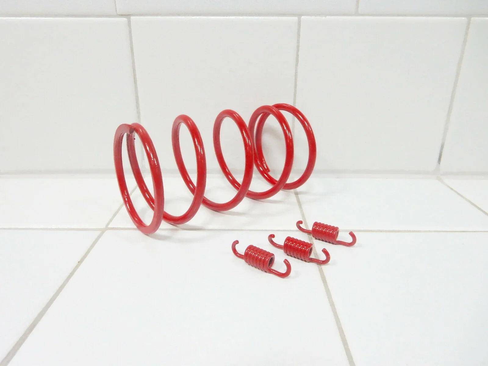 Red clutch spring set including one large coil spring and three smaller tension springs on white tile background