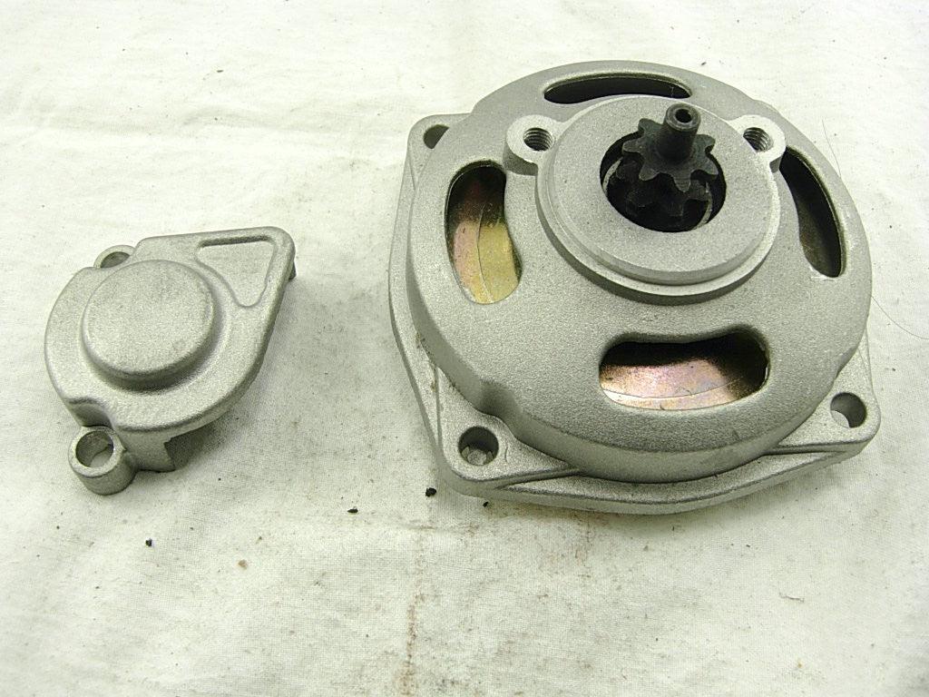 Two silver metal automotive parts on a white fabric surface, one round with gear teeth, the other smaller and compact