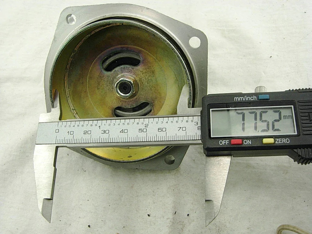 Digital caliper measuring 77.52 mm diameter of a round metal mechanical part on white surface