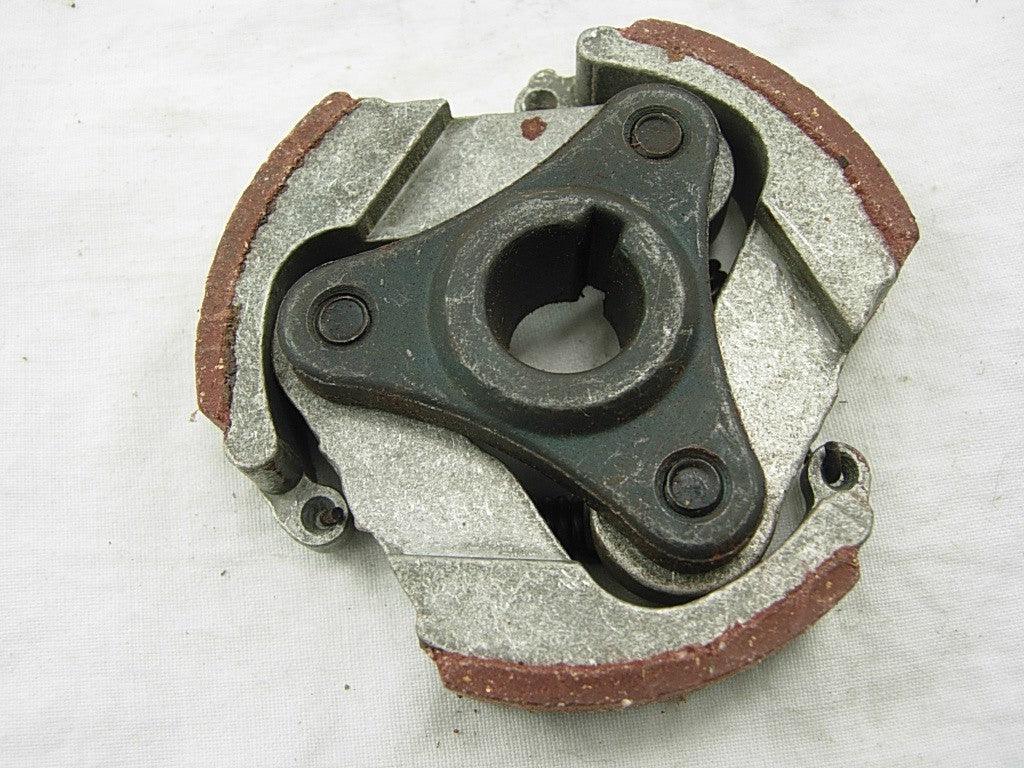 Close-up of a metal centrifugal clutch with three shoes and brown friction material on a white background
