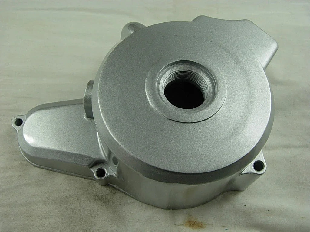 Silver metal engine crankcase cover with threaded central hole on beige surface