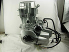 Silver motorcycle engine with black wires on white fabric background in studio setting