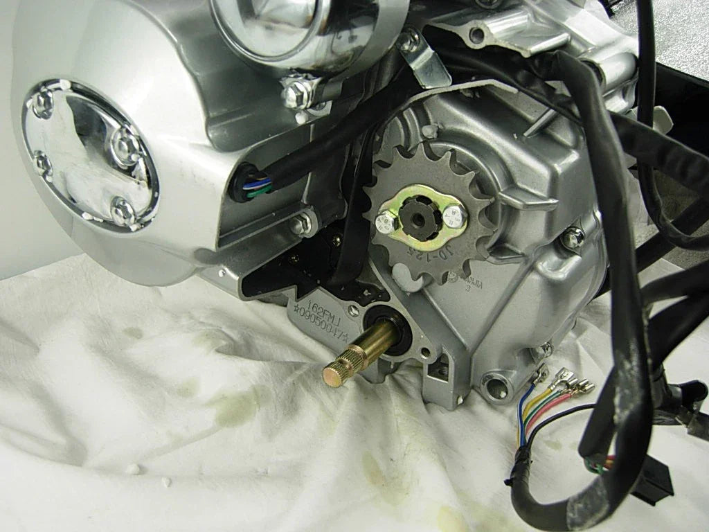 Close-up of silver motorcycle engine with visible sprocket and black wiring on white cloth
