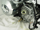 Close-up of silver motorcycle engine with visible sprocket and black wiring on white cloth