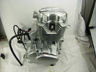 Silver motorcycle engine with cooling fins and black wiring on white fabric background