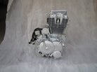 Silver motorcycle engine with cooling fins and attached wiring on gray fabric background