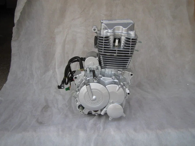 Silver motorcycle engine with cooling fins and attached wiring on gray fabric background